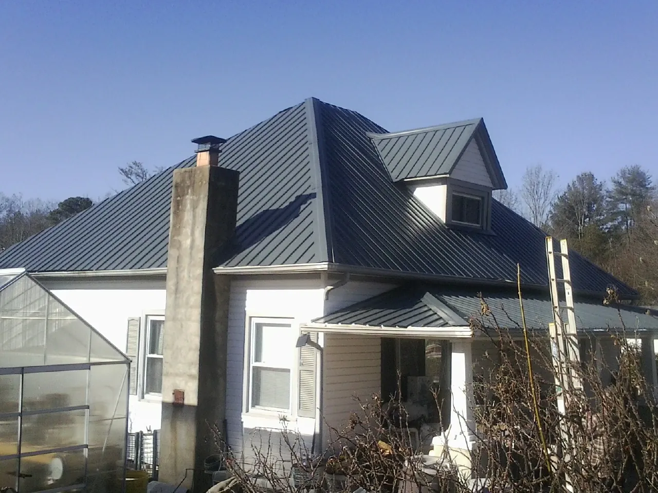 Dark blue standing seam metal roof on a white farmhouse with dormer — Slate & Tile Roof Repair by Roofing Brothers in Luck