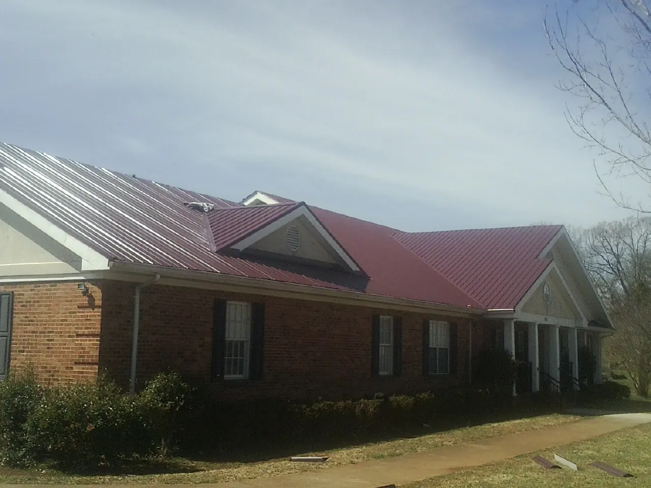 Red metal roof with gabled entries on a long brick building, from a Hail Damage Roof Repair job in Luck