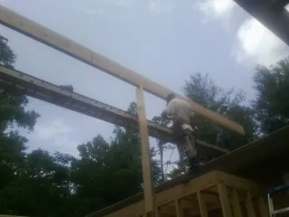 Carpenter setting a ridge beam over a new addition frame in Luck