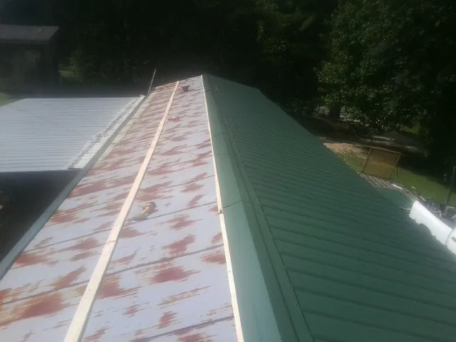 Old rusted panels beside newly installed green metal roofing — Wind Damage Roof Repair by Roofing Brothers in Luck