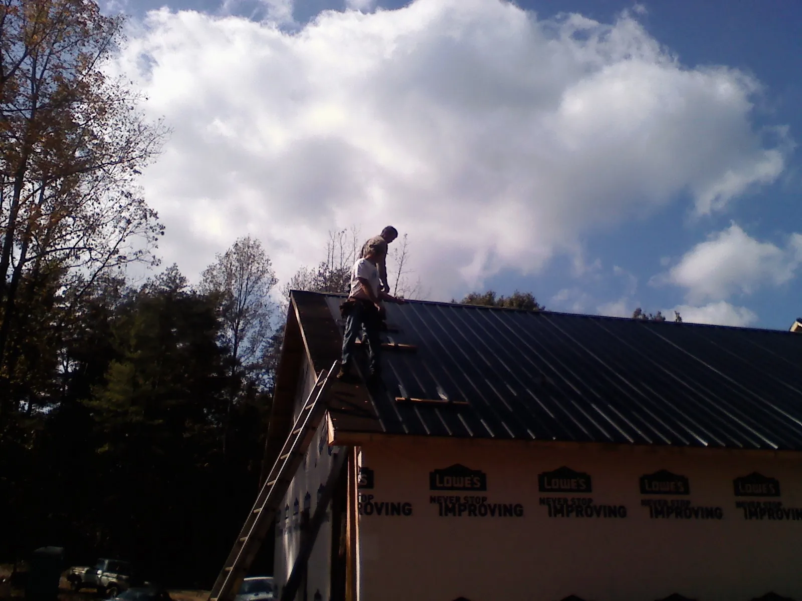 Roofer fastening dark metal panels high against a cloudy sky, from a Roof Inspection job in Luck